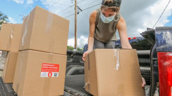 A woman wearing a mask loads boxes onto a truck.